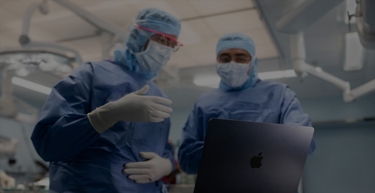 Two surgeons in scrubs looking at a MacBook Pro in the operating room.